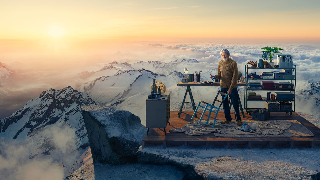Image of man on mountain top painting a chair